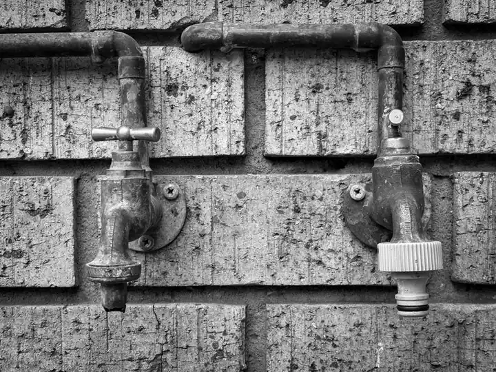 Close-up of vintage outdoor plumbing taps on a brick wall, black and white.
